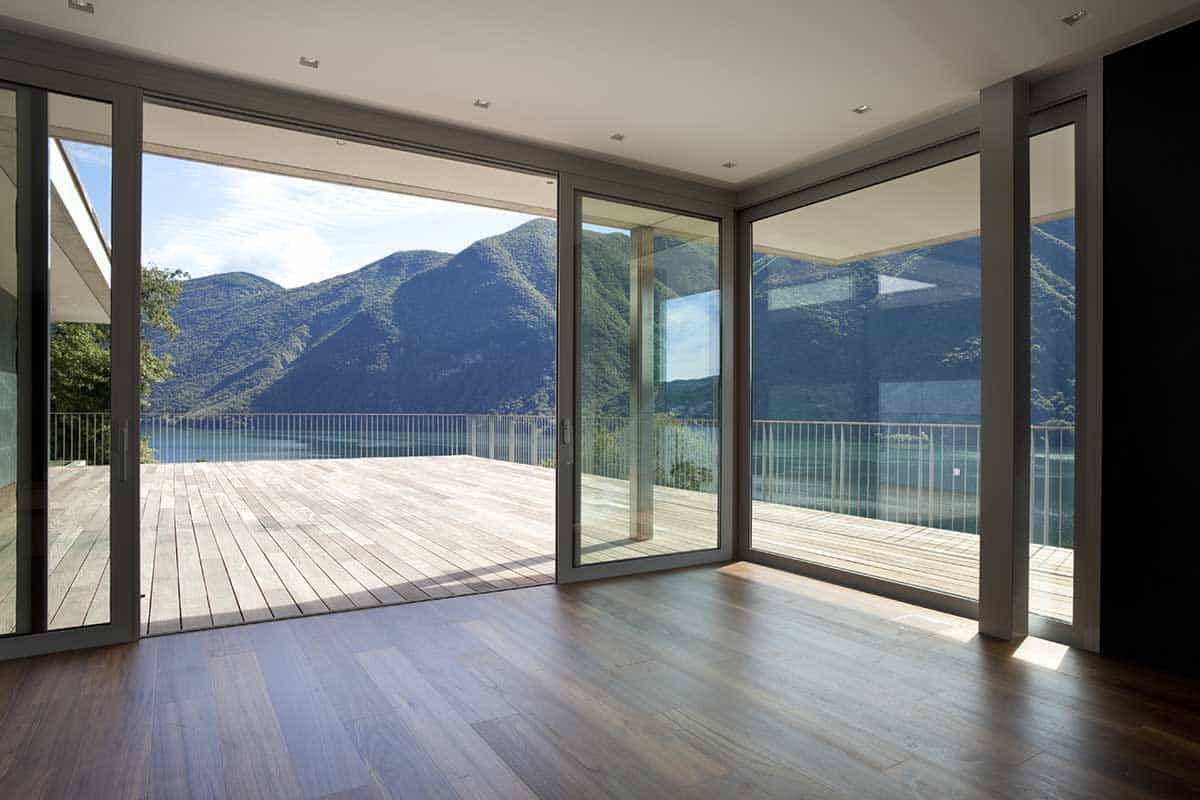 AdobeStock_27125894 - alexandre-zveiger Große Eckfenster mit Schiebeelement vom Wohnzimmer zur Terrasse mit Aussicht auf einen See