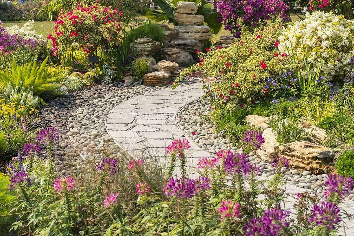 Ein Gartenweg aus Natursteinplatten mit vielen blühenden Blumen