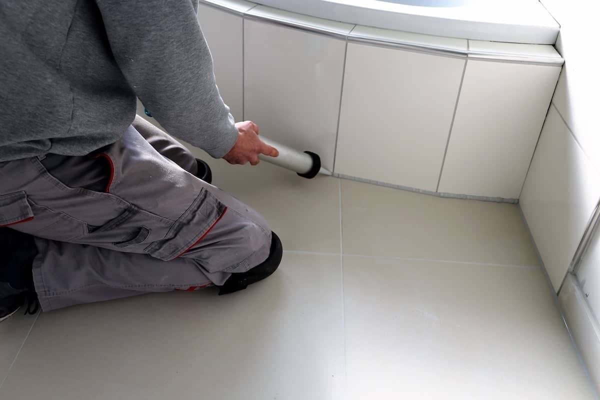 Ein Handwerker verfugt Fliesen im Badezimmer