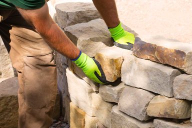 Ein Maurer baut im Garten eine Trockenmauer aus Naturstein