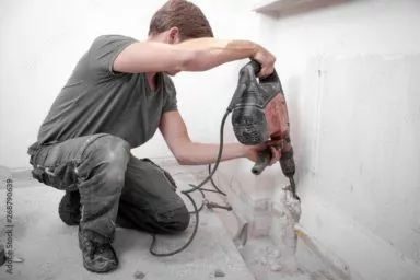 Ein Arbeiter stemmt eine Wand mit dem Bohrhammer auf. In Eigenleistung schafft er so die Öffnung für eine Heizungsleitung.