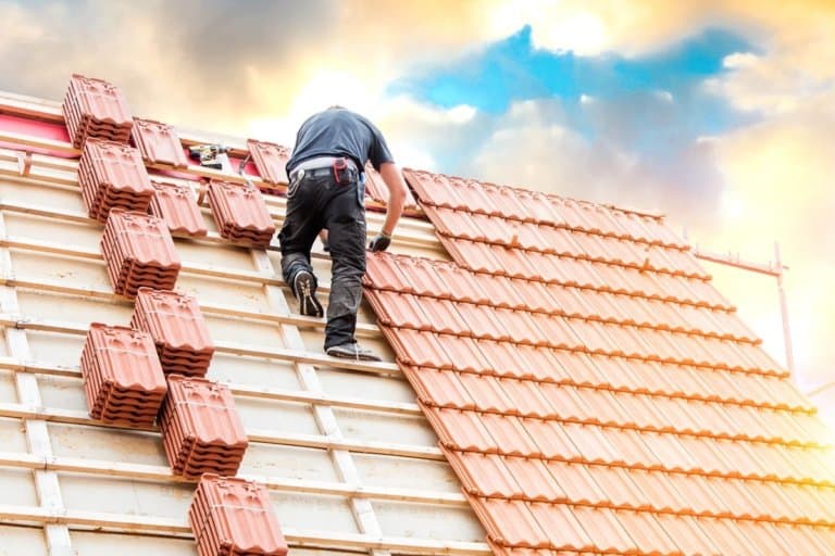 Dachdecker auf dem Dach mit Dachziegelstapeln